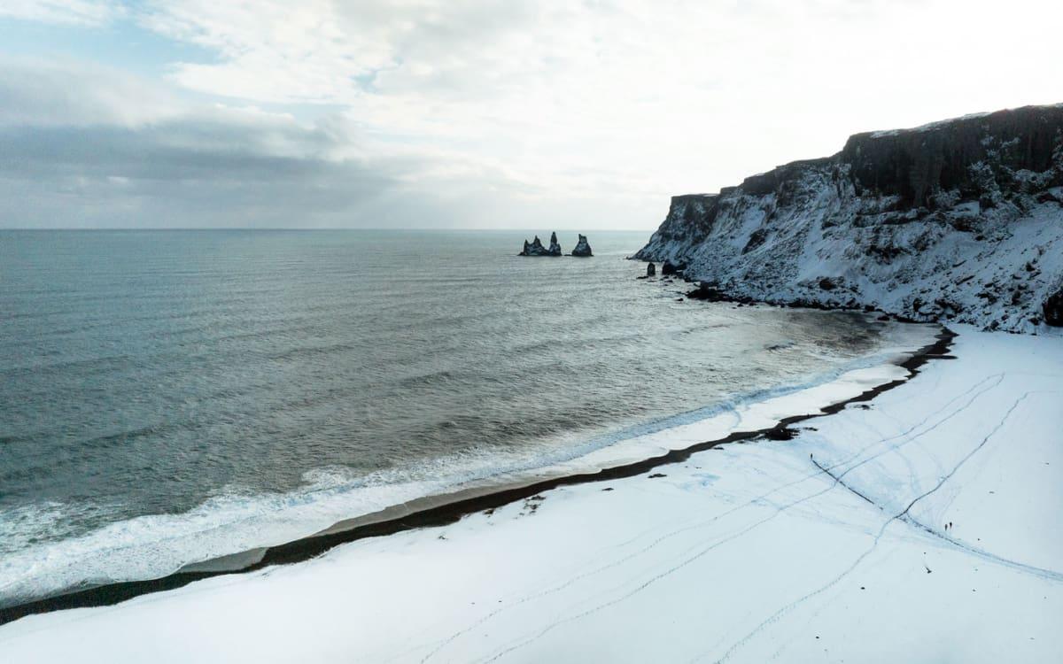 Black sand beach in Vik with a view of the famous basalt columns covered with snow